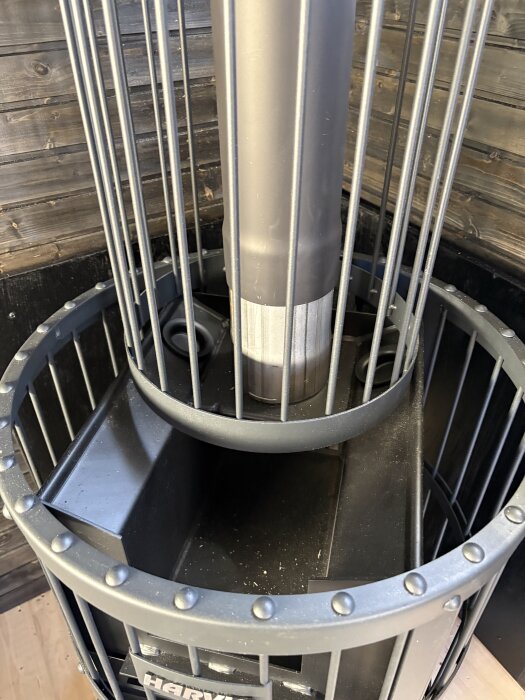 Bastuugn med metallgaller runt, placerad mot en trävägg.