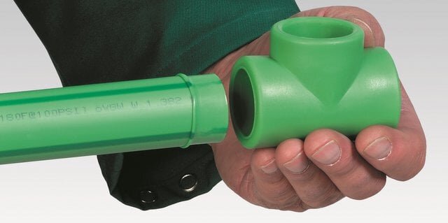 Grönt rörsystem "Aquatherm" med ett handhållet T-rör och rak rördel, svetsade för skarvfri installation.