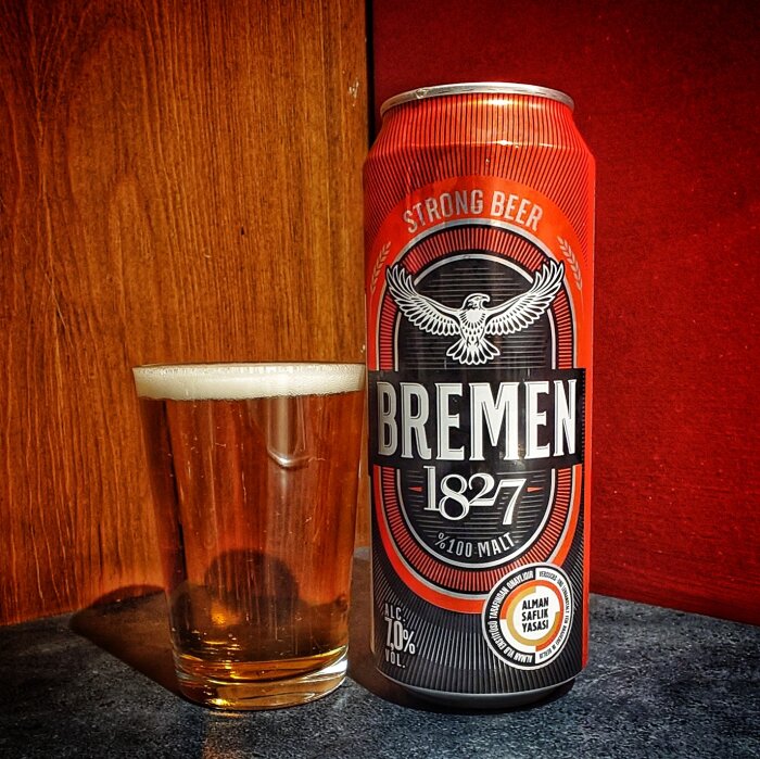 En röd ölburk märkt "Bremen 1827 Strong Beer" bredvid ett fyllt ölglas på ett bord.