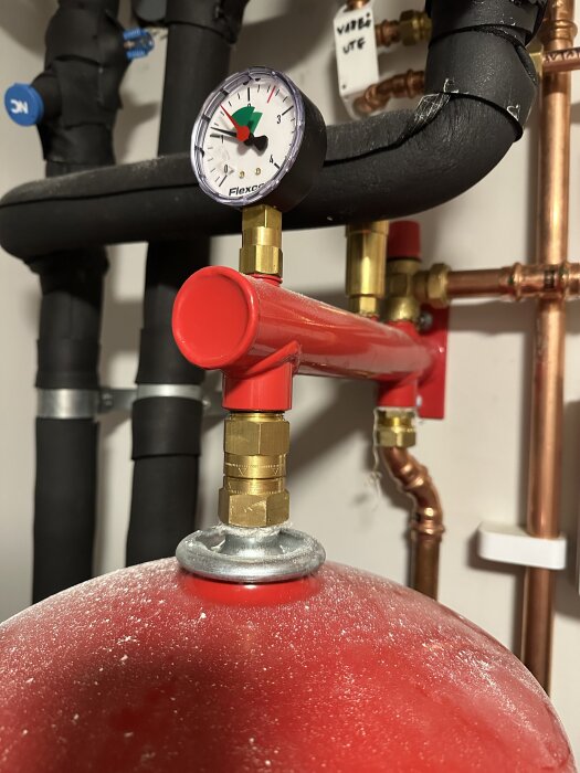 Manometer på ett rörsystem visar tryck med en nål som pekar utanför det gröna området. Röda ventilen används för att justera trycket.