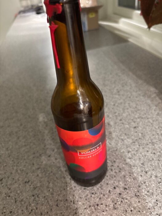 Flaska med etikett från Põhjala Cellar Series på en stenbänkskiva, omgiven av mjuk belysning.