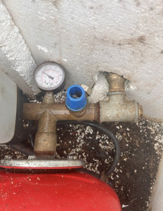 Manometer och blå ventil bredvid röranslutning i ett vattensystem, med en tryckströmbrytare och röd tank synlig längst ner.