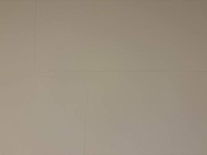 Sprickor längs skarvarna på innerväggar av gipsskivor i ett hus, både lodrätt och vågrätt, cirka 1 mm breda.