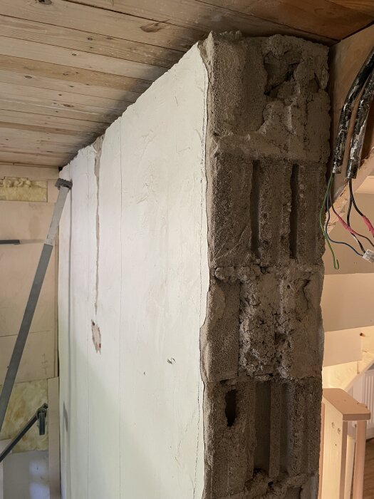 Vägg med gammalt putslag bredvid obehandlad yta, trätak ovan, kabeldragning till höger; diskussion om renovering med gips och tapet.