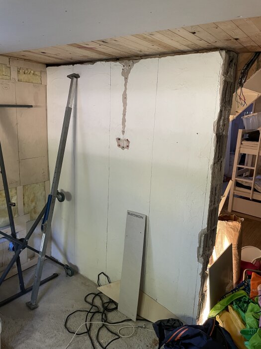 Renoveringsprojekt: Delvis riven innervägg med putsad yta och exponerade kanter, omgiven av byggmaterial och verktyg.