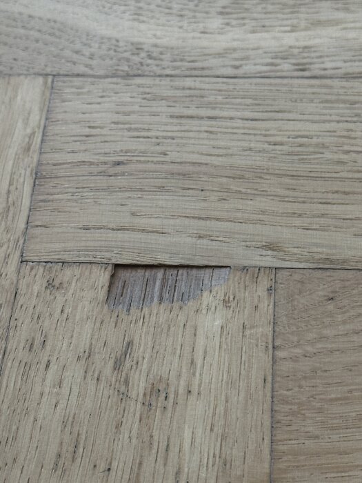 Fiskbensparkett med saknad flisa i ett vardagsrumsgolv; fråga om att fylla med woodfiller eller kemiskt/plastiskt trä.