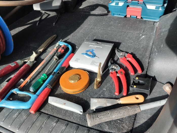 Olika verktyg som såg, limpistol, skruvmejsel, avbitartång och sekatörer ligger i bagageutrymme, fyndade på loppis.