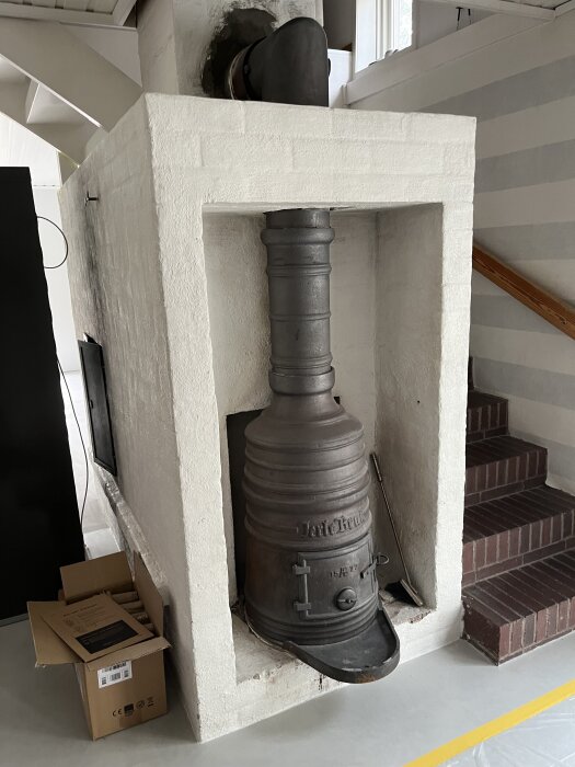 Vit putsad konstruktion med en gammal svart kamin och skorsten placerad intill en trappa i ett modernt hem.