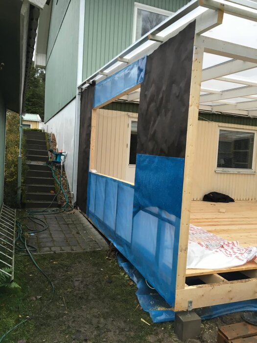 Byggprojekt med plastfolie fastsatt på utsidan av en trästomme, samt oavslutade paneler.