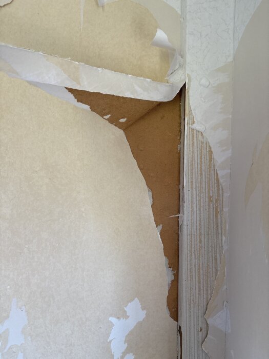 Rivit tapet i ett sekelskifteshus, delvis exponerad masonit och tapetrester på väggen i vardagsrum under renovering.