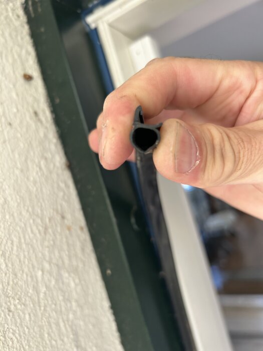 En hand håller en U- eller D-formad gummilist intill en dörrkarm, troligen för att hantera sågspån i karm.