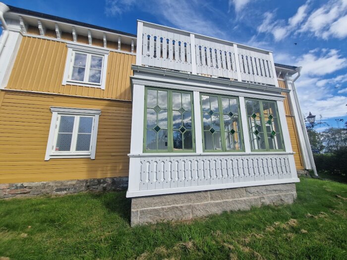 Gul träfasad med en vit och grön veranda med rombformade fönster, före renovering.