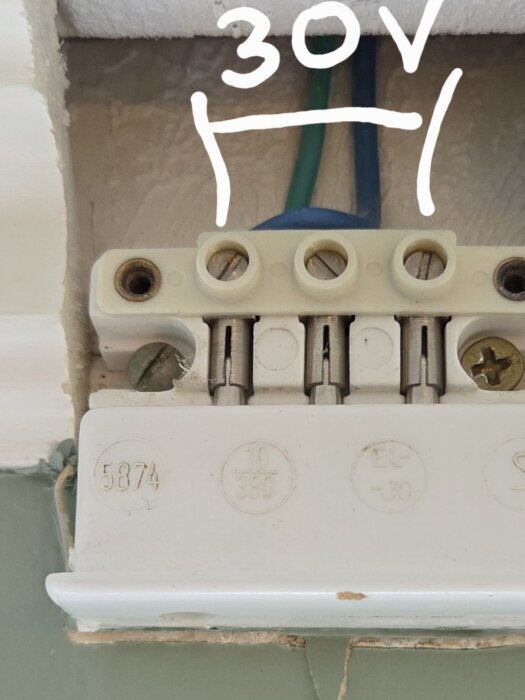 Elektrisk dosa med synliga ledningar, infälld i taklist. Mätvärden noteras med 30V mellan två yttre ledare. Installationen är från ett radhus byggt 1975.