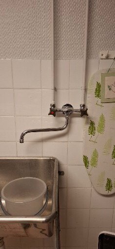 Väggmonterad tvättställsblandare med två vred och pip över diskho, flankerad av ett strykbräda i tvättstuga.