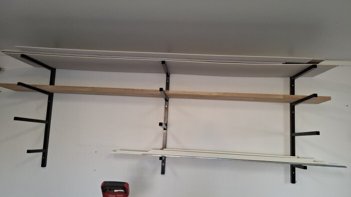 Väggmonterad virkesförvaring i garaget med svetsade metallkonsoler och hyllplan.