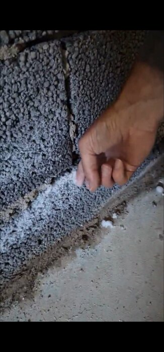Hand vid källarvägg med vit utfällning i lekablock, eventuell fuktproblem.