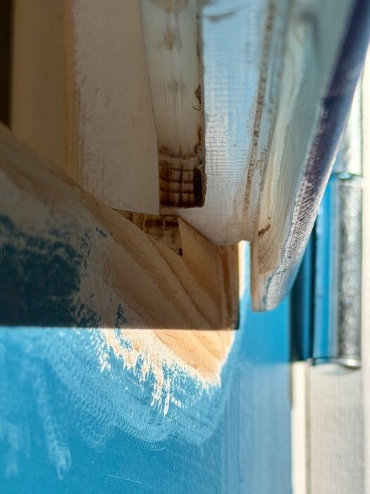 Närbild av fräsning på ytterfönsterram med nyslipade ytor och blå bakgrund, visar arbete med att förbättra fönstret.