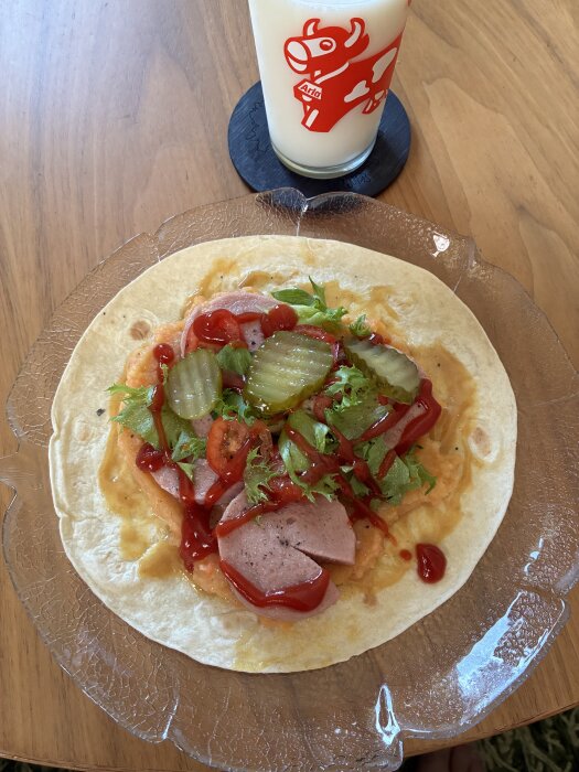Tunnbrödsrulle med tacobröd, rotmos, köttkorv, sallad, tomat, gurka, ketchup och smörgåsgurka på glasfat, intill ett glas mjölk.