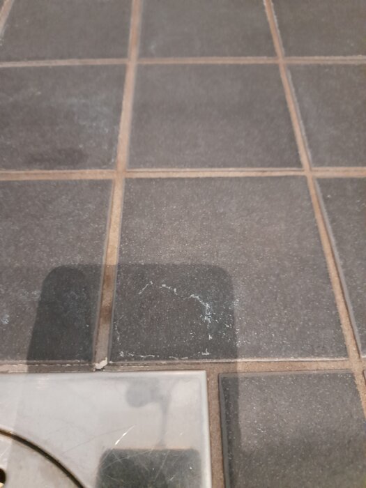 Brunt klinkergolv med vita fläckar i närheten av ett avlopp.