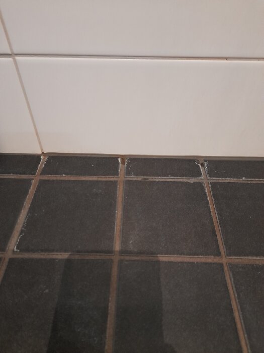 Vita fläckar på mörkt kakelgolv i badrum, möjliga kalkfläckar från handtvätt med flytande tvättmedel.