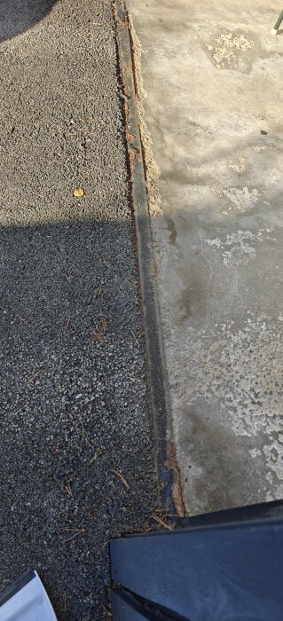 Garagegolv vid elport med en rostig metallist och sliten yta. Asfalt möter betonggolv, och viss smuts och skador är synliga.