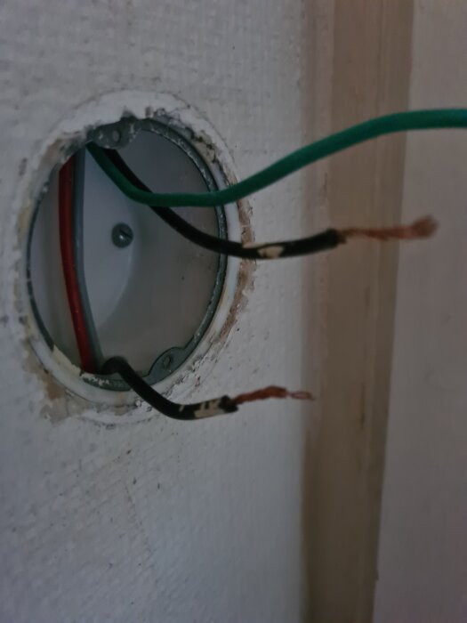 Oisolerade elektriska sladdar sticker ut från en rund väggöppning, redo att kopplas till en strömbrytare.