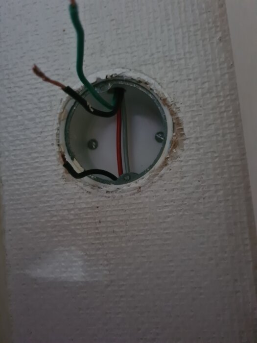 En rund elbox i väggen med synliga, oanslutna ledningar i olika färger: grön, röd och svart.
