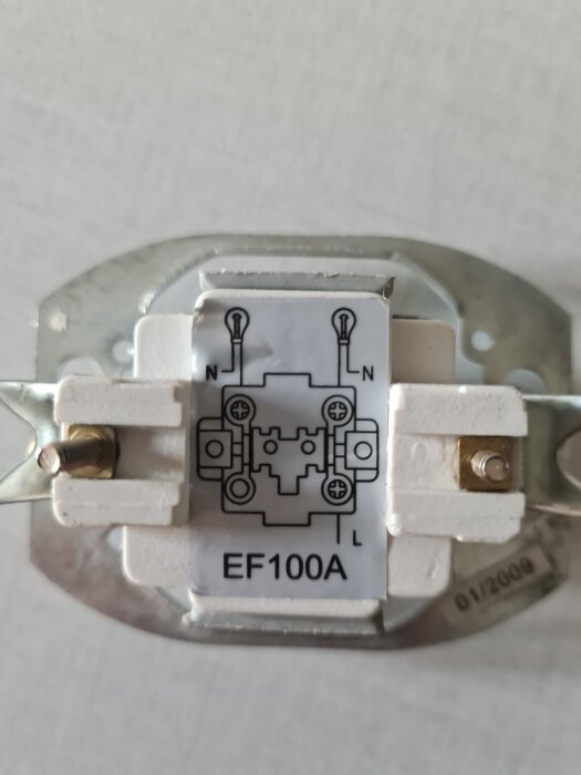 Bild på baksidan av en strömbrytare med en kopplingsschemaetikett, text "EF100A", samt N och L terminaler.
