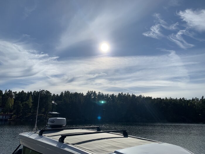 Båt under solig himmel i skärgården, med barrskog och vatten i bakgrunden.