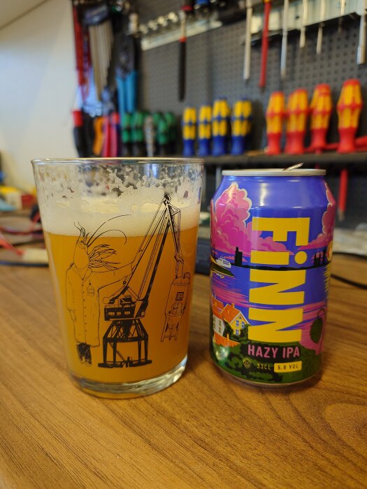 En ölglas med EPA-logga bredvid en burk Finn Hazy IPA på ett bord, verktyg synliga i bakgrunden.