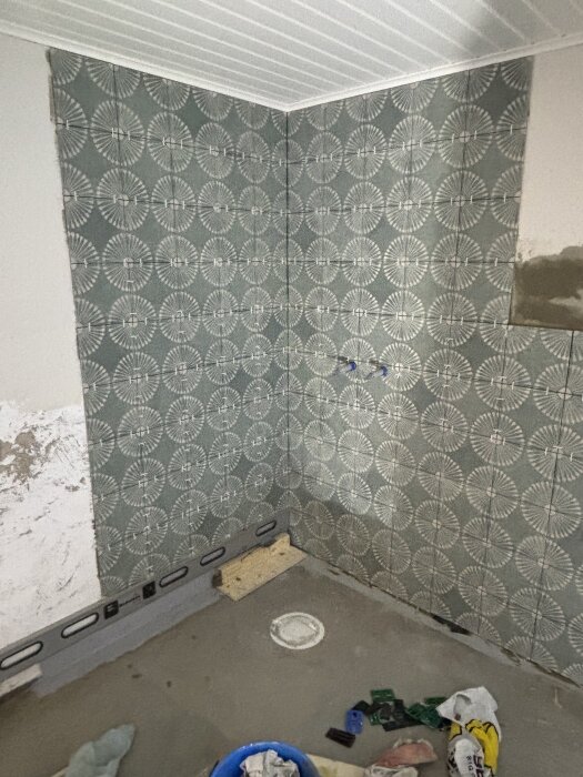 Pågående kakelsättning av vägg i rum med blå och vita kakelplattor, verktyg och material på golvet.