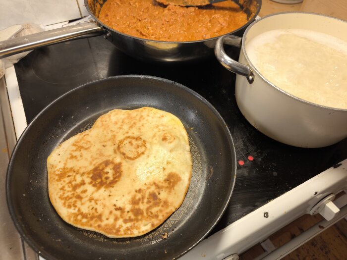 Stekpanna med Nanbröd, kastrull med ris och gryta med Chicken Vindaloo på en spis.