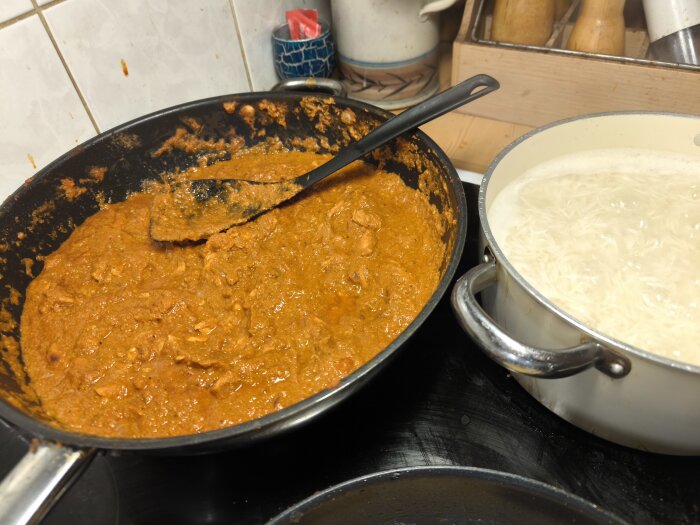 Chicken Vindaloo i stekpanna bredvid kastrull med kokande Basmati-ris i köket.