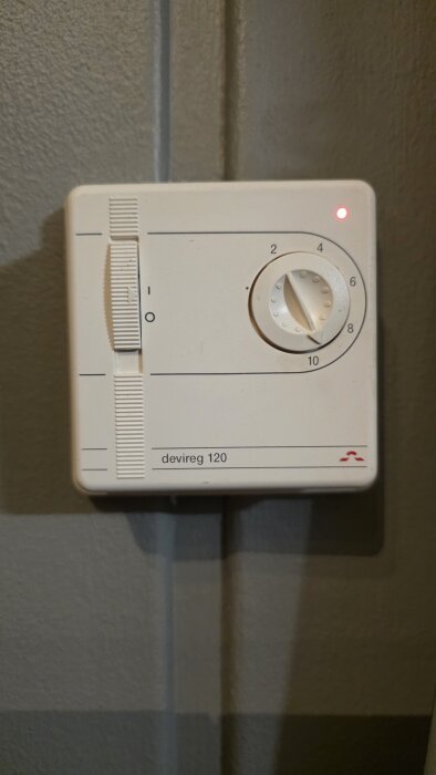 Termostat för golvvärme, modell devireg 120, monterad på vägg, med vridbar temperaturkontroll och rött ljus som indikerar driftstatus.