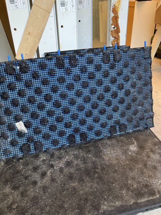 Begagnade gymmattor med blått mönster och svarta prickar, lutade mot en vägg inomhus.