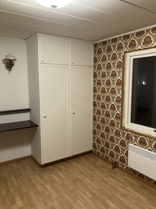 Sovrum med öppet utrymme, garderob, tapetserad vägg och element under fönstret.