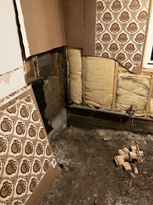 Sovrum under renovering med rivna väggar och blottad isolering samt en hög med byggmaterial på golvet.