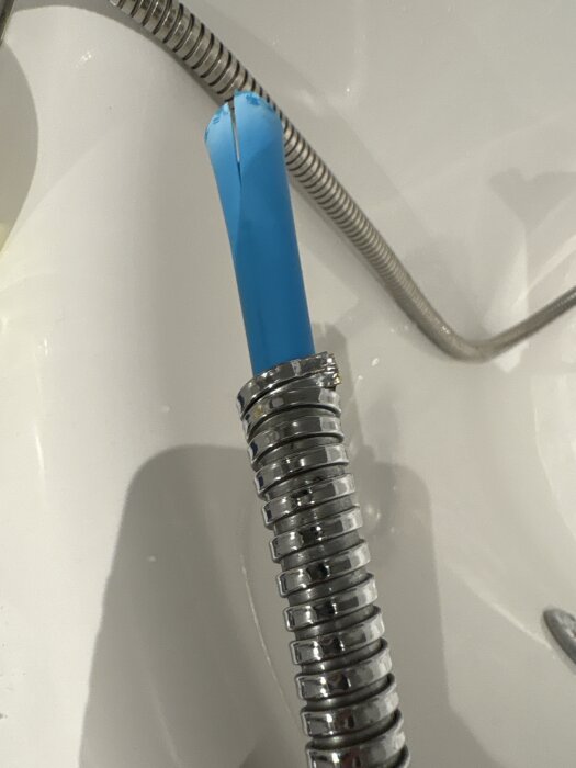 Trasig duschslang med avbruten spiral och synlig blå innerdel i badrum.