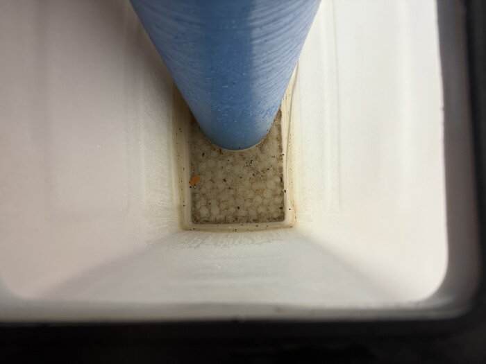 Inuti vit plastbehållare med blått rör i mitten, smutsigt botten med mögel och smuts runt kanterna.