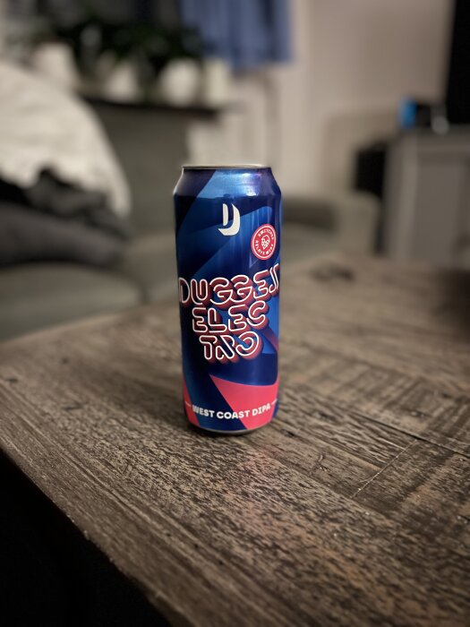 En burk med öl märkt "Dugges Electro" West Coast DIPA står på ett träbord inomhus.