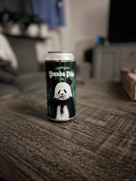 Burk med "Panda Pils" öl, dekorerad med en pandaillustration, står på ett träbord i en inomhusmiljö.