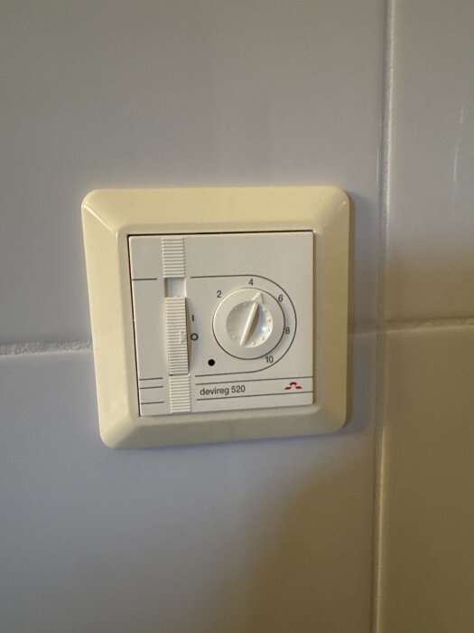 En Devireg 520 golvtermostat monterad på en kaklad vägg.