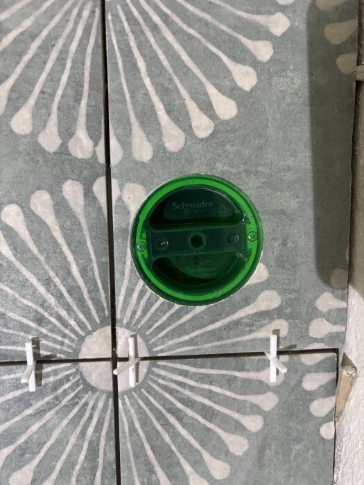 Gröna Schneider Electric-cover på mönstrad kakelvägg, med perfekta hål, skapade med diamant hålsågar för vinkelslip.