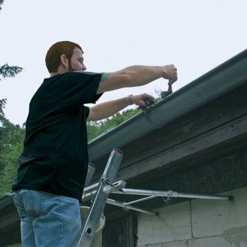 Man står på stege och justerar takränna med hjälp av avståndshållare.