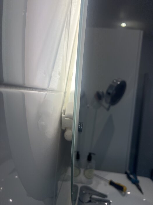 Närbild på en badrumsspegel med belysning bakom, synliga verktyg som skruvmejsel och tång på handfatet.