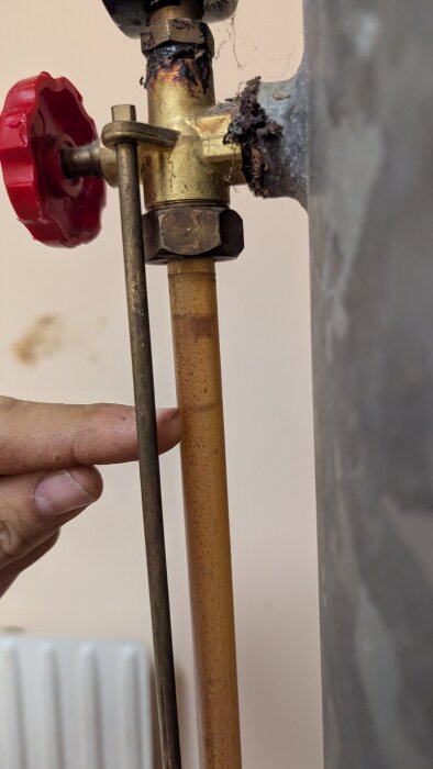 Gammal ventil med röd vred-förslutning och korroderat mässingsrör som visar tryckproblem i vattenledningar enligt diskussionstråd.