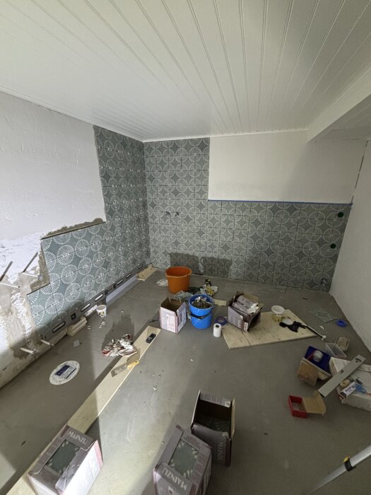 Renovering av rum med tapetserad vägg, verktyg och byggmaterial spridda på golvet.