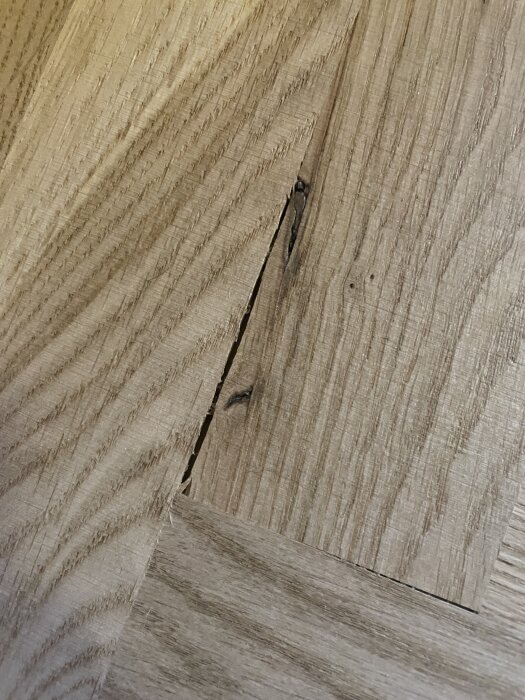 Fiskbensparkett med springor mellan stavarna och en trasig bit, visar bristfällig installation och kvalitetsproblem i golvläggningen.