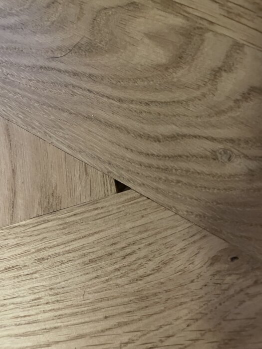 Fiskbensparkett med glipa mellan stavar och trasig bit, visar brister i golvläggningen.