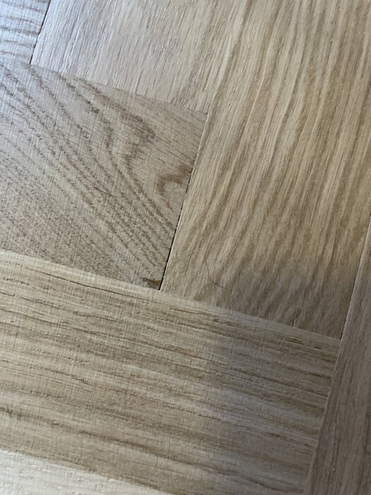 Fiskbensparkett med glipor mellan stavarna och en ojämn yta synlig efter slipning.
